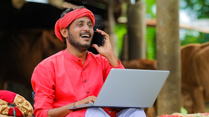Young Indian farmer talking on mobile phone and using laptop at home.