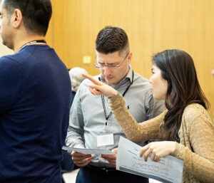 Woman pointing in a classroom whilst a colleague reads from a sheet of paper.