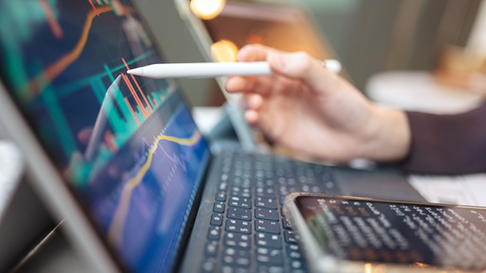 Pointing at an laptop screen showing financial graphs.