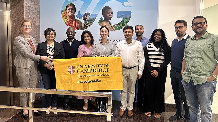 Executive MBA classmates stand together behind a Cambridge Judge banner.