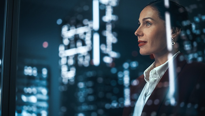 Businesswoman looking out at nighttime skyscrapers.