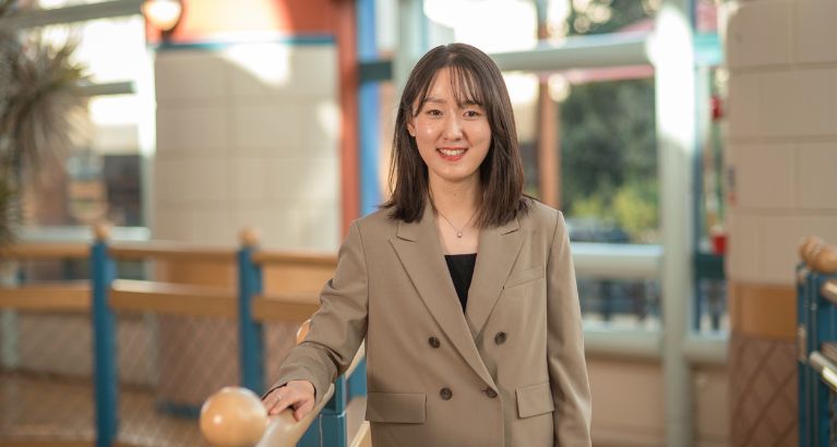 Seoil Jang smiling and standing in front of Cambridge Judge Business School staircase