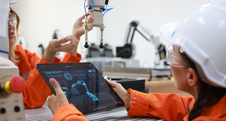 Female maintenance engineer using a digital tablet beside an industrial robotic arm in a manufacturing facility.