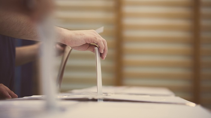 Hand placing a vote in a ballot box.