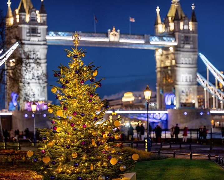 A beautiful illuminated Christmas tree in front of the iconic Tower Bridge of London, England, during winter night time.