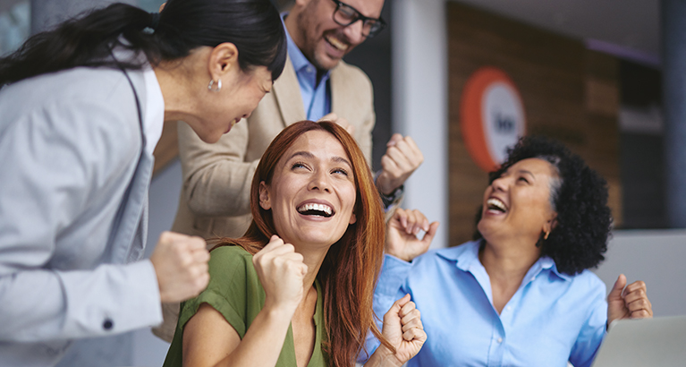 A diverse group of four colleagues celebrating a success in an office setting.
